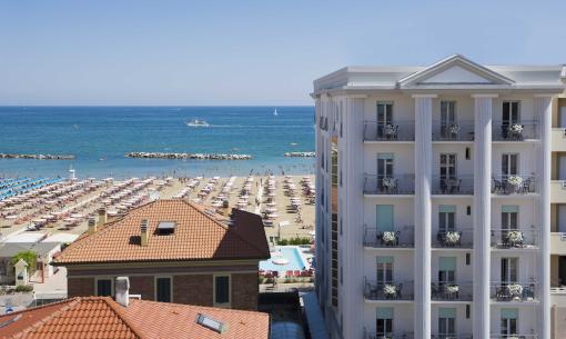 Spiaggia affollata con ombrelloni e mare blu, vista da un edificio.